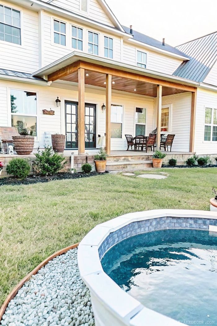 Modern home with white siding features a small round above ground pool with stone border, surrounded by pebbles and lush landscaping.