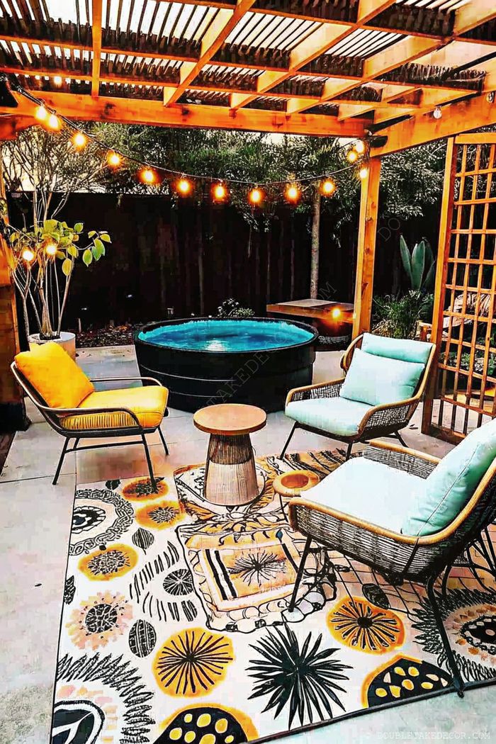 Cozy outdoor space with a hot tub under a wooden pergola strung with lights, complemented by stylish seating and tropical rug.