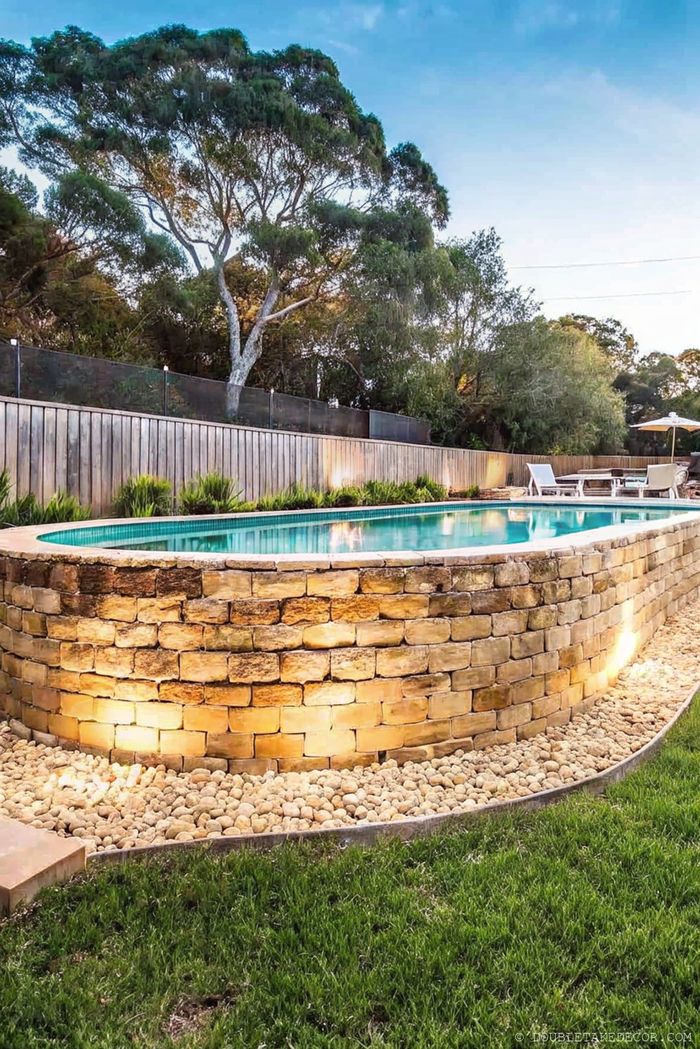 Circular above ground pool with rustic stone wall surround, soft lighting, and lush landscaping creating a serene outdoor retreat.