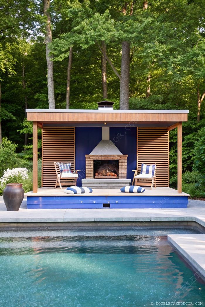 Elegant outdoor space featuring a stone fireplace flanked by wooden chairs with plaid cushions, beside a serene pool surrounded by greenery.