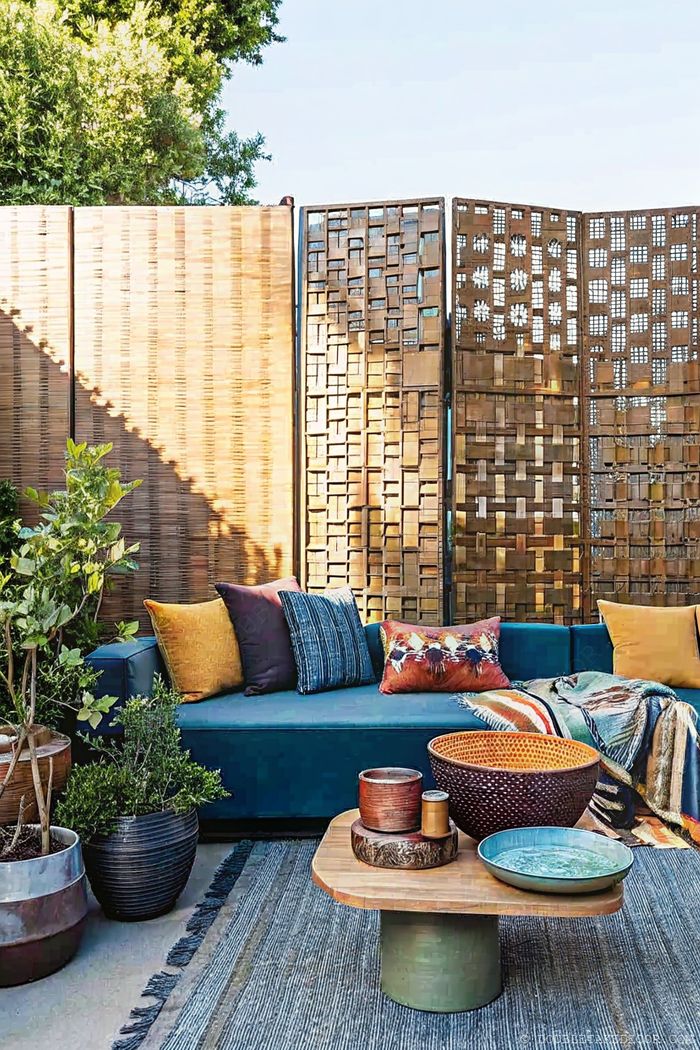 Blue sectional sofa with pillows, coffee table, and woven privacy screen in an outdoor lounge setting with potted plants