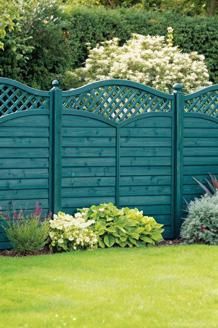Teal wooden fence with lattice detailing surrounded by lush greenery and flowering plants for backyard privacy