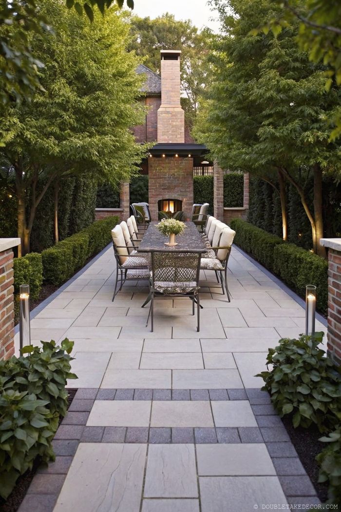 Private outdoor dining area with hedged pathways, stone patio, and background fireplace for entertaining neighbors