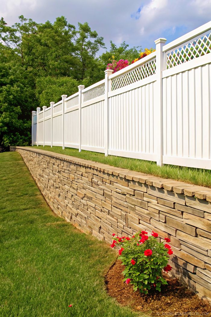 White vinyl fence with decorative lattice top provides privacy while complementing a landscaped garden with colorful flowers.