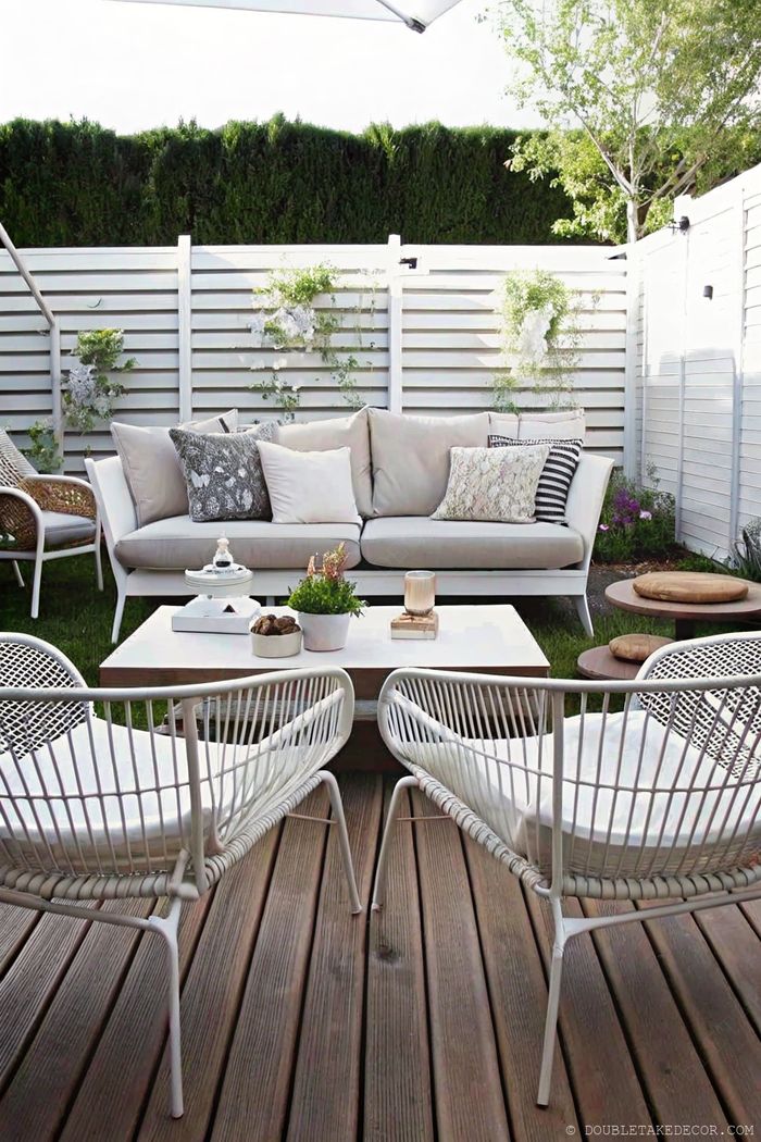 Modern outdoor living space with light gray sofa, wire chairs, and white slatted privacy fence for backyard seclusion.