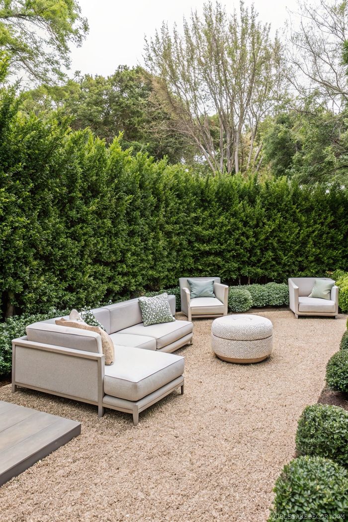 Secluded outdoor living space with gray sectional sofa, armchairs, and ottoman, surrounded by privacy hedges