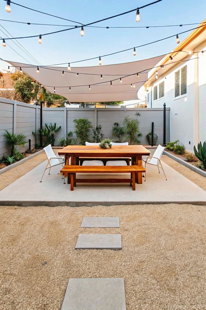 Contemporary outdoor dining area with sail shade, string lights, and privacy fence surrounded by strategic landscaping.