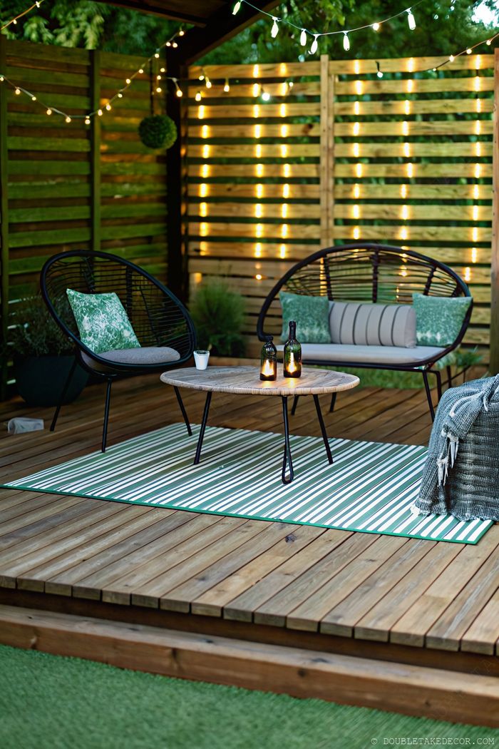 Intimate outdoor seating area with black chairs, wooden privacy slats, string lights, and green accents for backyard privacy