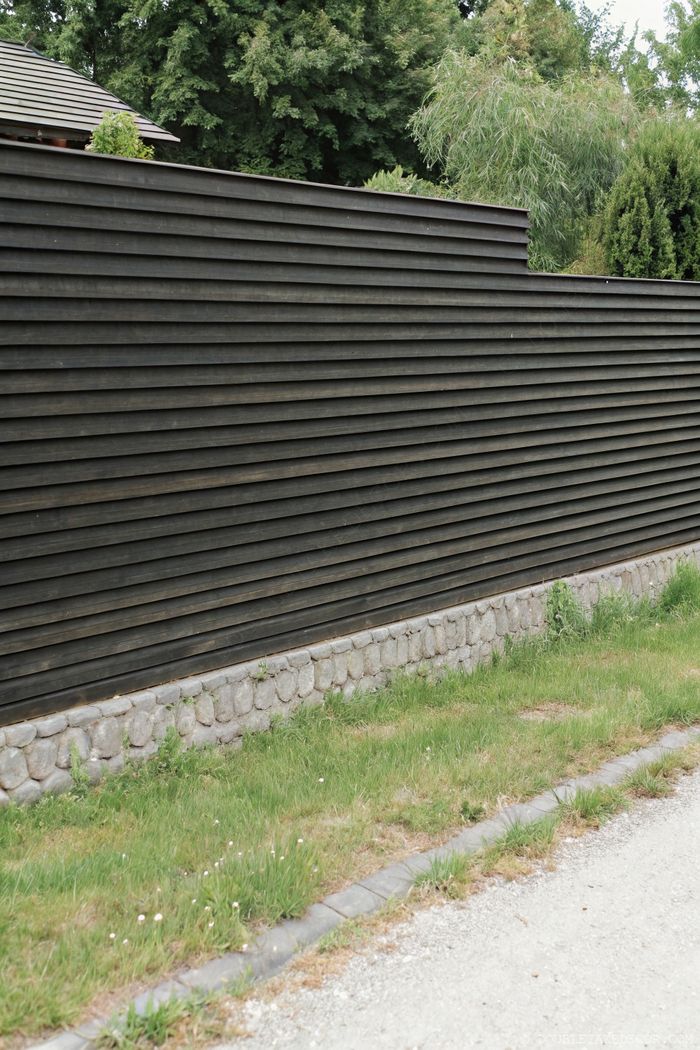 Modern dark wooden horizontal slat fence with stone foundation providing sleek, contemporary privacy in a landscaped yard