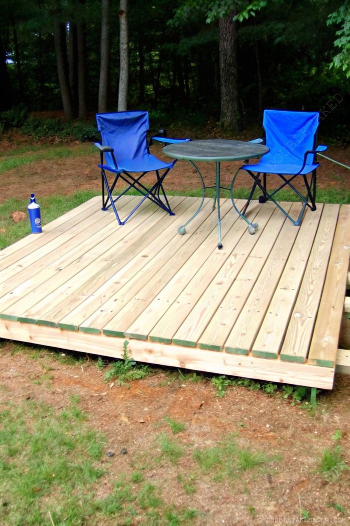 Petite terrasse en palettes dans un cadre naturel avec deux chaises pliantes bleues autour d’une table ronde, parfaite pour la détente extérieure.