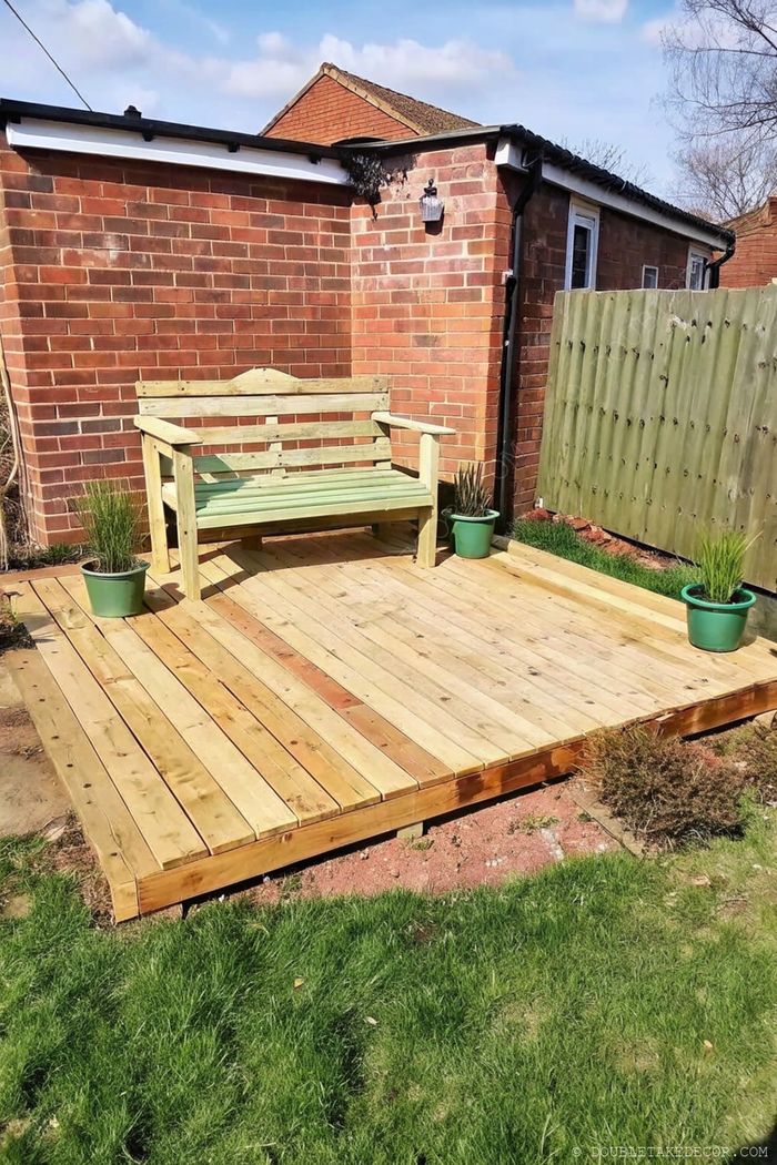 Terrasse DIY en palettes avec lames claires, banc peint en vert, et plantes en pot devant un mur en briques.