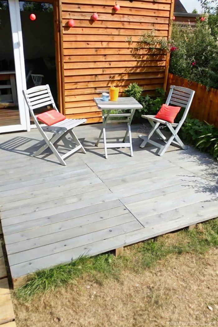 Petite terrasse en palettes avec fauteuils aux coussins orange et pot de fleurs jaune, parfait pour les coins détente extérieurs.