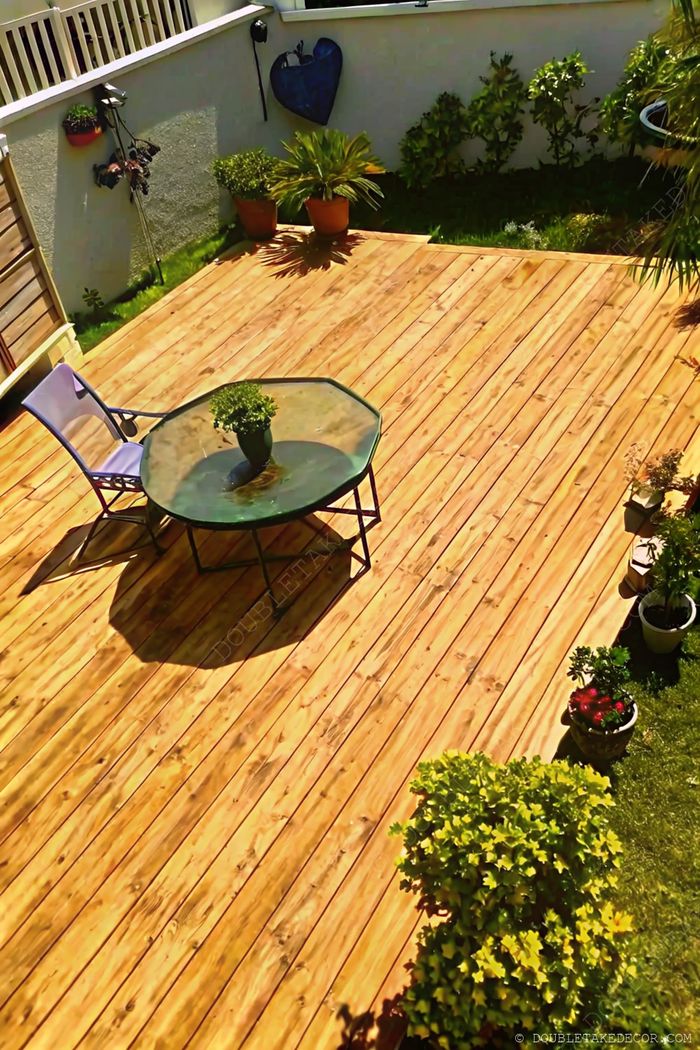 Terrasse extérieure accueillante en bois avec table en verre octogonale, chaise violette, et plantes en pot tout autour, créant un coin détente chaleureux