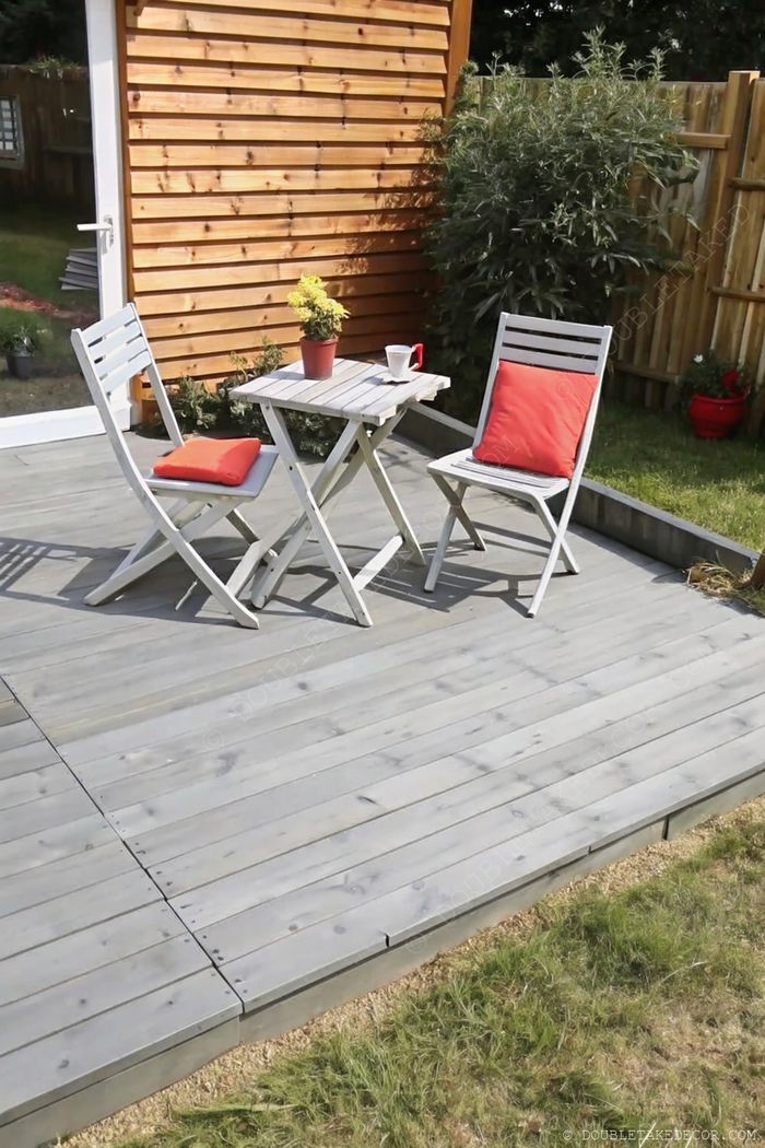 Petite terrasse intime en palettes avec chaises pliantes blanches, coussins rouges et table en bois décorée d’une plante jaune, parfaite pour la détente.