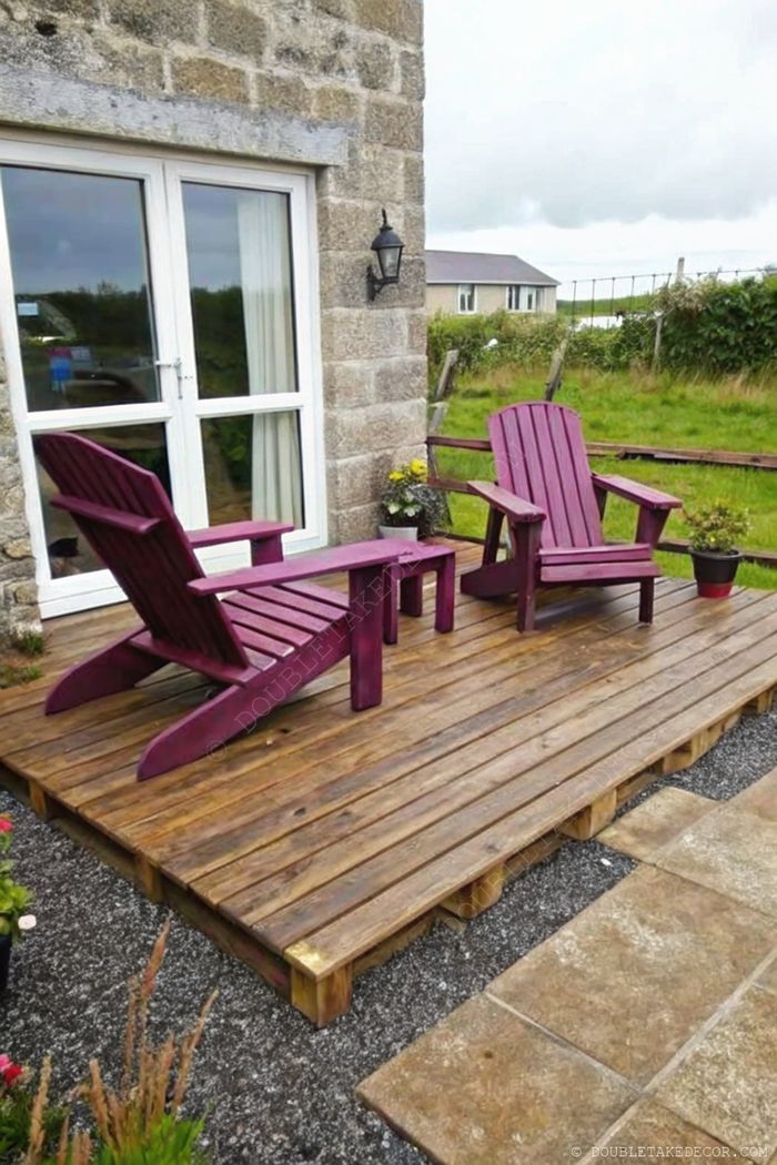 Coin détente extérieur avec deux chaises Adirondack violettes et table assortie sur terrasse en bois, entouré de verdure.