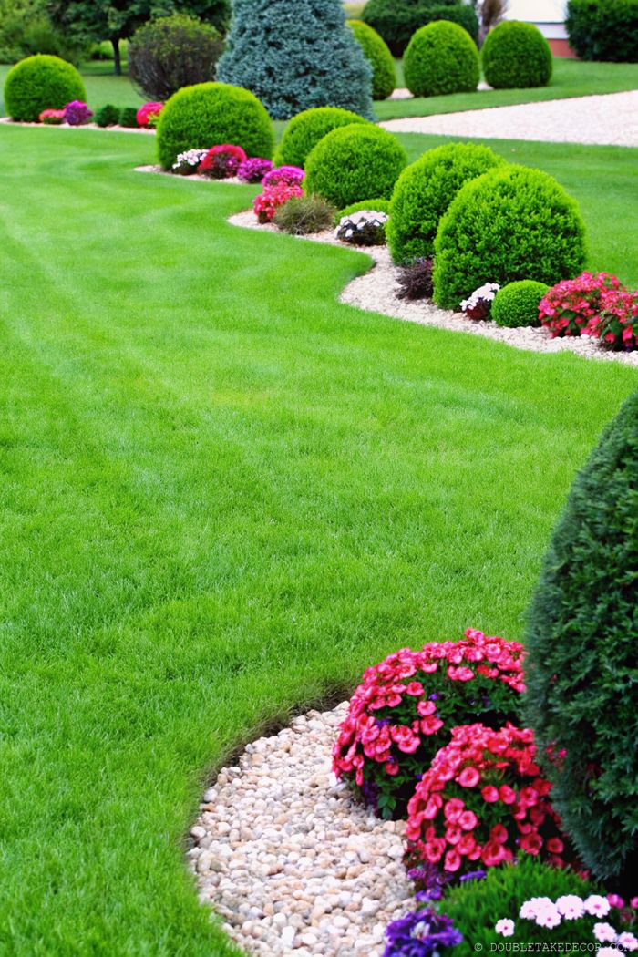 Eleganter Garten mit geschwungenen Rändern, die dichten Rasen von bunten Blumenbeeten und runden Sträuchern mit Kieswegen trennen.