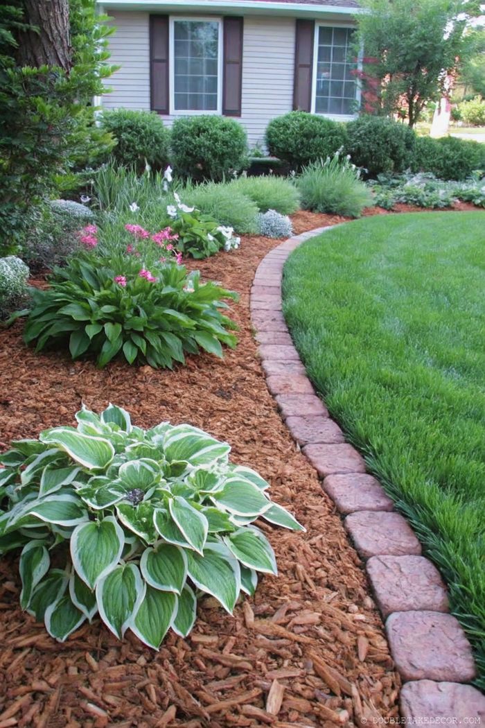 Angelegter Garten mit geschwungenem Steinweg zwischen Blumenbeeten mit Hostas, rosa Blüten und dunkler Mulchschicht, die den Eingangsbereich verschönern.
