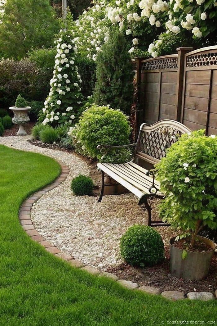 Ruhiger Garten mit geschwungenem Kiesweg, umgeben von dichtem Rasen, einer Holzbank, Formschnittbüschen und blühenden Sträuchern.