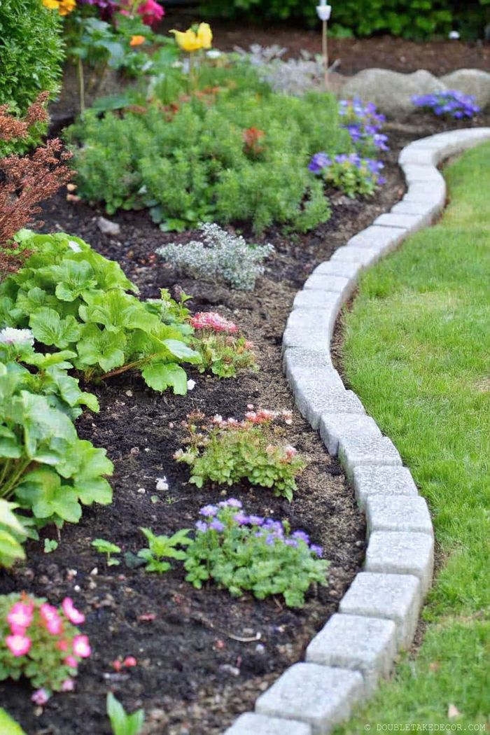 Gartenbeet mit geschwungener Steinumrandung trennt farbige Blumen von der Rasenfläche. Zu sehen sind pinke, violette und gelbe Blüten.