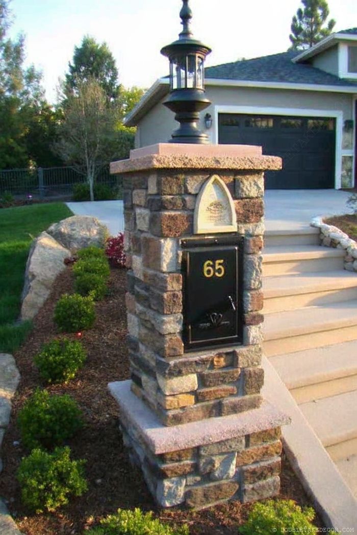Elegant mailbox on stone pillar with decorative lantern, displaying golden address numbers and surrounded by manicured landscaping.