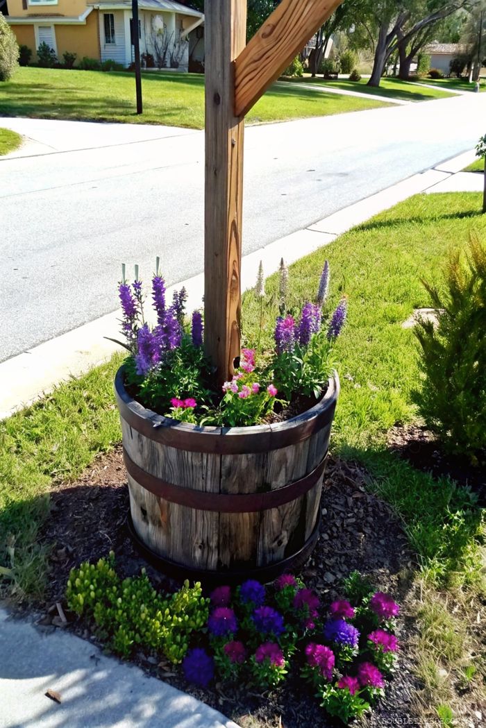 Repurposed wooden barrel planter filled with purple larkspur and pink flowers, creating a colorful landscape accent for mailbox area.