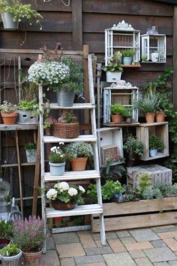 Charming vertical garden with white ladder plant stand against wooden fence, displaying colorful flowers in various pots and wooden crates