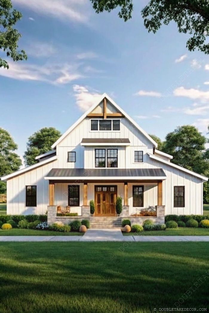Farmhouse-stílusú barndominium fehér burkolattal, nyeregtetővel, nagy ablakokkal és tágas elülső verandával fa oszlopokkal, parkosított kertben.