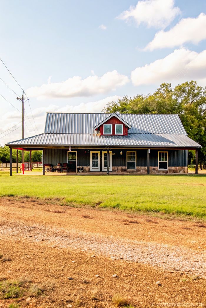 Bájos, modern farmhouse fém tetővel, faburkolatokkal, sötét oldalfallal, piros kiemeléssel a tető oromzatán, és barátságos tornáccal, természetes környezetben.