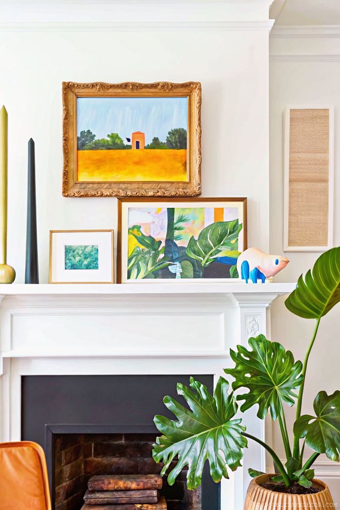 Eleganter Sommer-Kaminsims mit gerahmten Bildern, Kerzen und einer großen Monstera als grüner Blickfang – für ein modernes, behagliches Highlight.