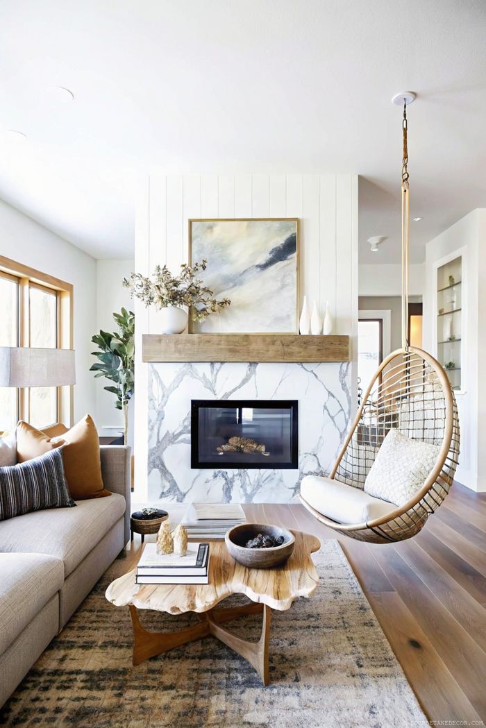 Modernes Wohnzimmer mit schwarzem Kamin vor Marmorwand, dazu Holzregale, Naturdeko und Sommerpflanzen.