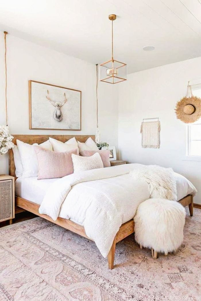 Inviting bedroom with white and blush bedding, wooden headboard, rustic deer artwork, minimalist nightstands, and cozy textiles creating a tranquil retreat.