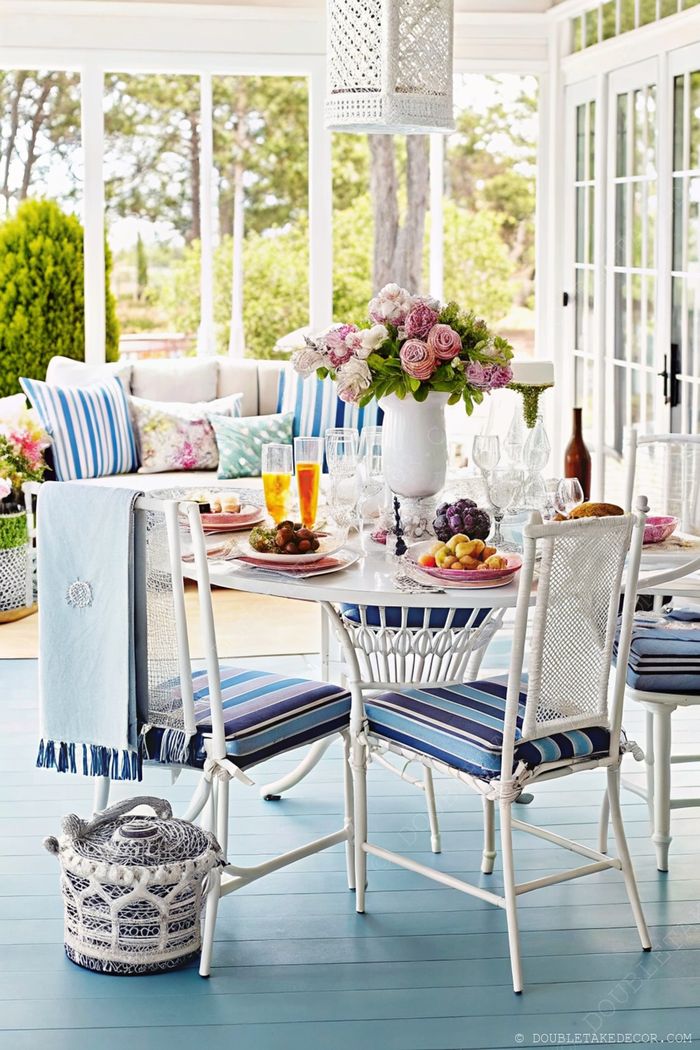Bright dining area with round white table, pink roses centerpiece, and blue-striped cushions creating a serene coastal atmosphere.