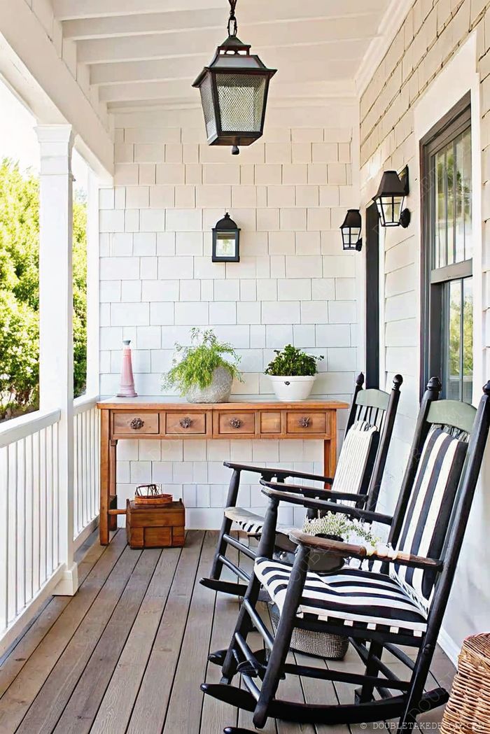 A cozy porch with black rocking chairs, white clapboard walls, and a rustic wooden console table adorned with potted plants.