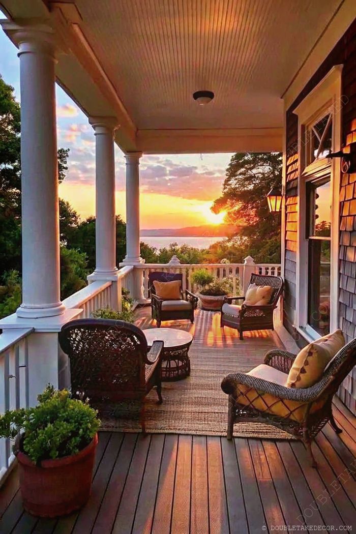 Cozy porch with wicker chairs and cushions around a table, illuminated by warm sunset light over water view.