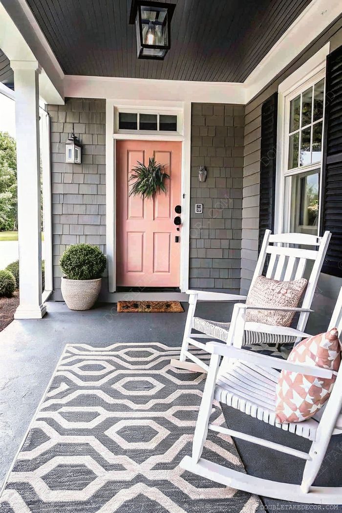 Cozy front porch featuring a pink door with wreath, white rocking chair, geometric area rug, and decorative planter for a stylish entryway.