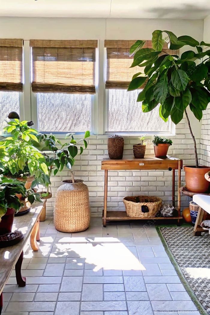 Véranda transformée en paradis de plantes avec de nombreuses espèces, table en bois rustique, paniers de rangement tressés et stores en bambou.