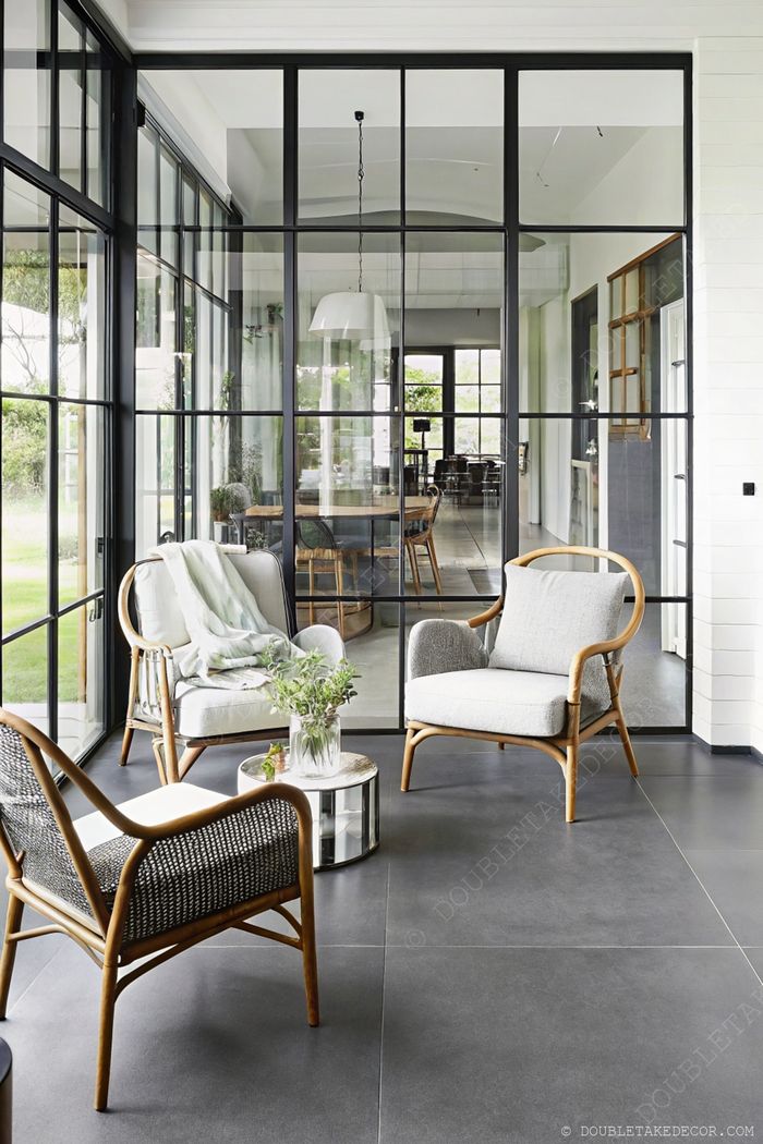 Véranda avec grandes baies vitrées à cadres noirs, deux fauteuils élégants et table miroir pour un espace détente moderne et lumineux.