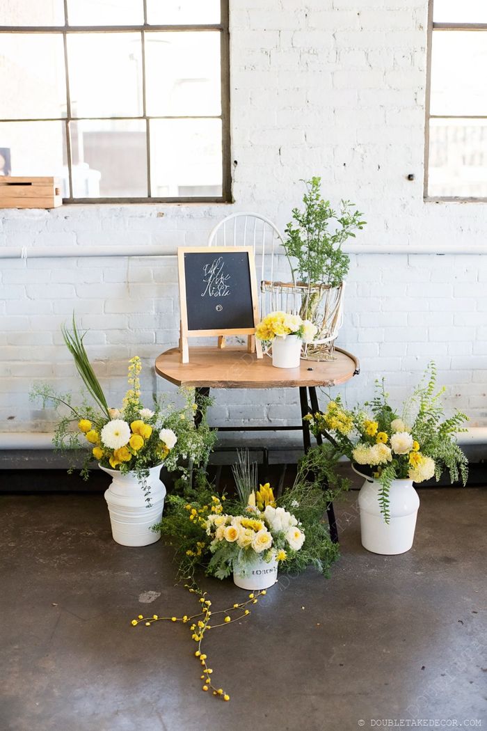 Charming flower bar with wooden table, potted yellow and white flowers, chalkboard sign and rustic chair against white brick walls