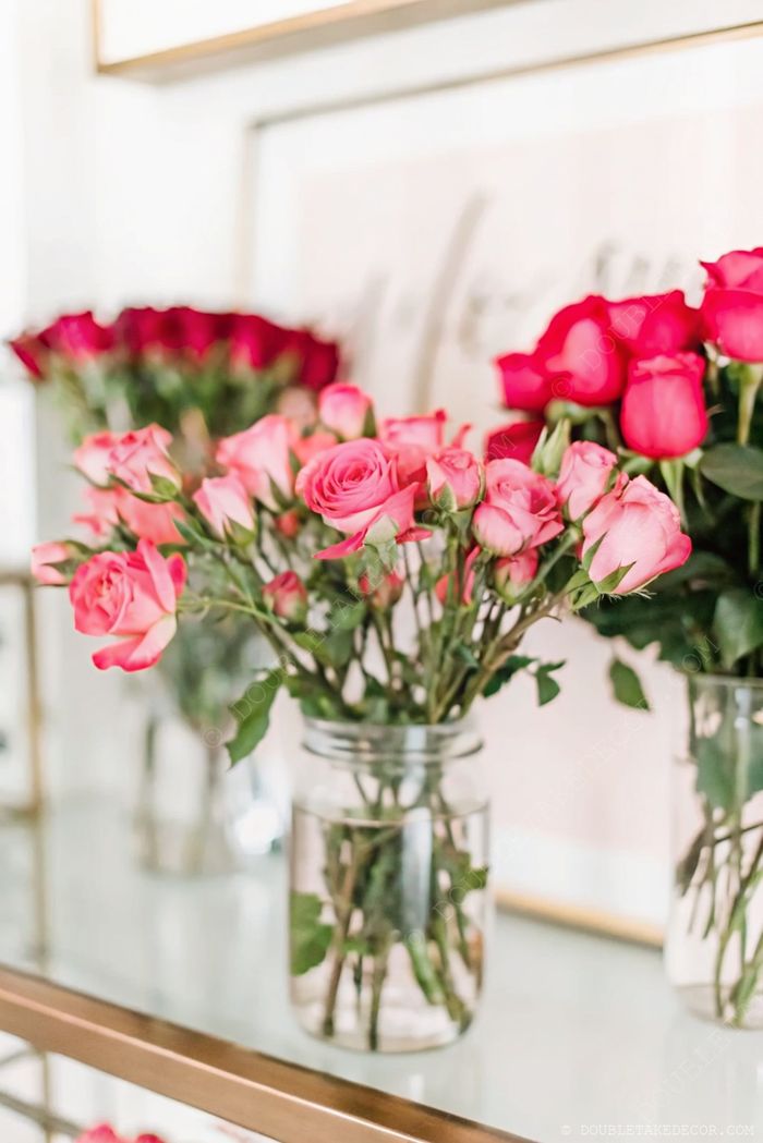 Pink and dark red roses arranged in transparent glass jars, showcasing stems and leaves for a fresh DIY flower bar centerpiece