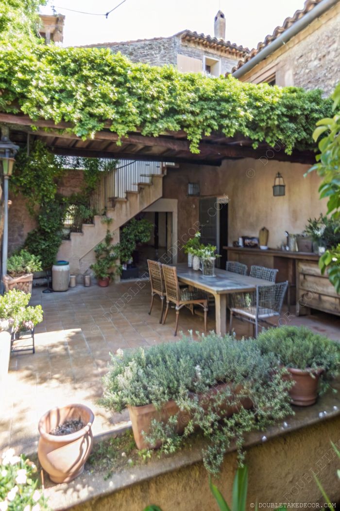 French garden patio with wooden pergola covered in vines, featuring wicker dining furniture and herb planters for a serene outdoor retreat.
