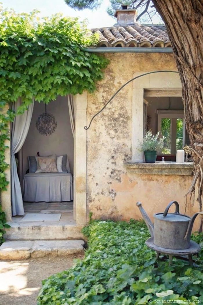 Charming outdoor nook with curtained archway, cozy bed, and pendant light amid weathered walls and cascading vines - perfect French garden sanctuary.