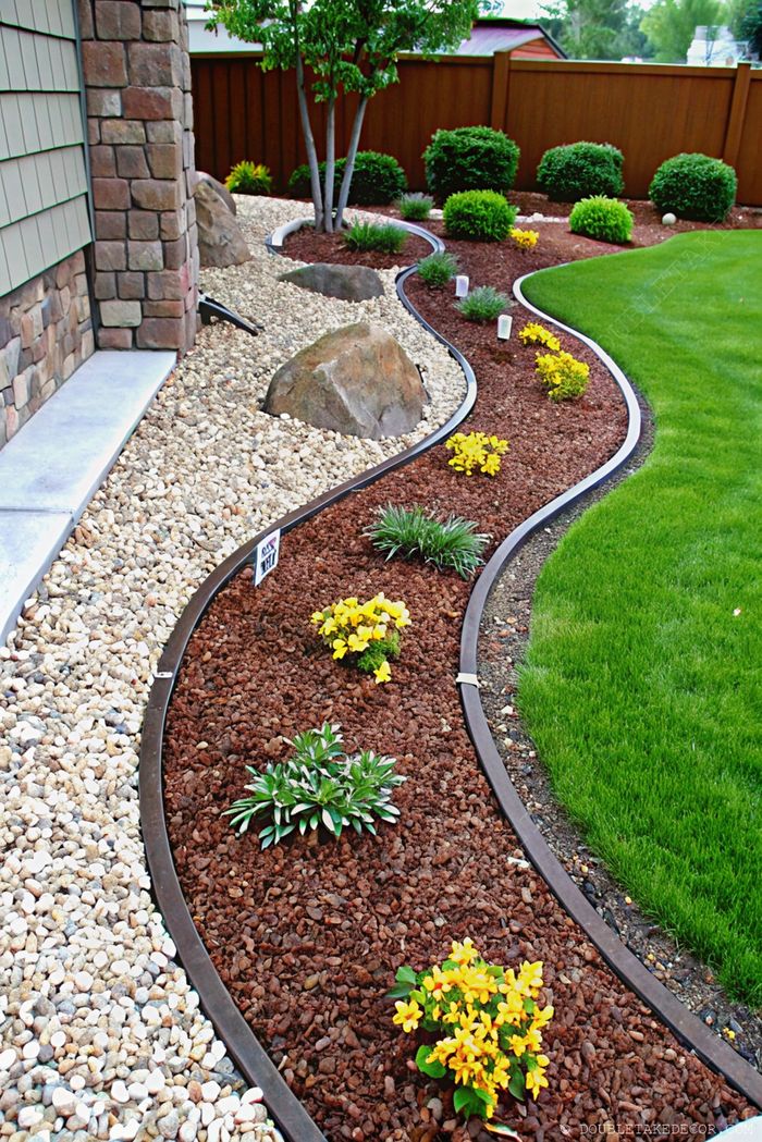 Beautifully landscaped garden with curved gray stone pathway, gravel accents, vibrant yellow flowers in mulched beds, and clean edging.