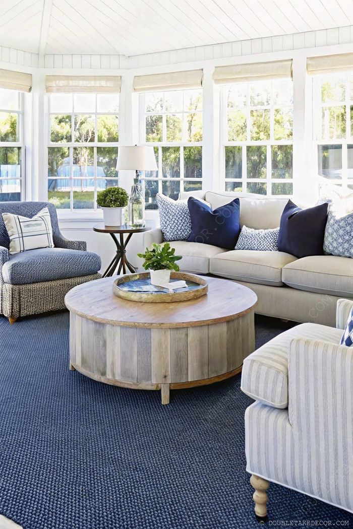 Heller Wintergarten mit L-förmigem Sofa, blauen Sesseln, Holztisch, viel Licht durch weiße Gardinen.