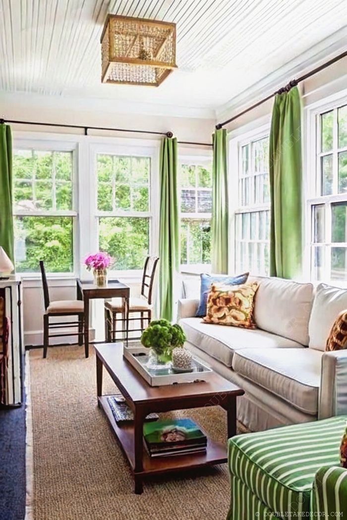 Heller Wintergarten mit vertäfelter Decke, weichem Sofa, grün gestreiftem Stuhl, Holztisch und kleinem Essbereich an großen Fenstern.