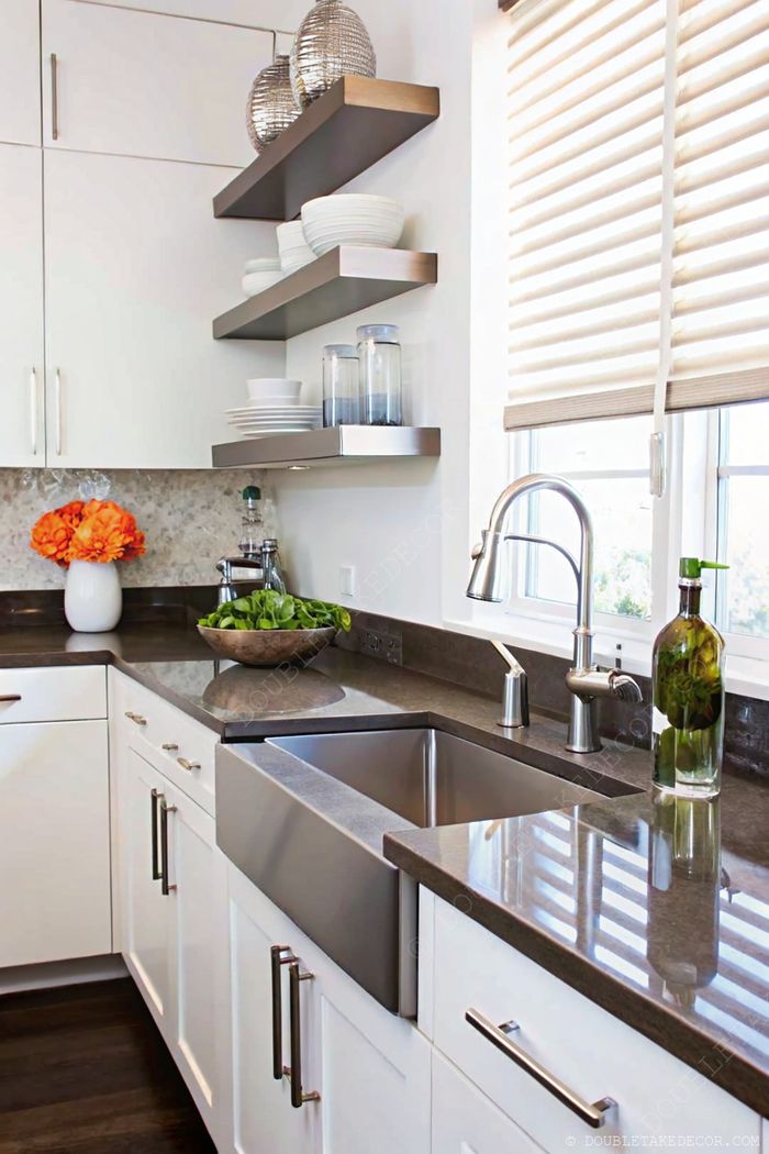 Modern kitchen with white cabinets, dark granite countertops, open metal shelves displaying dishes, and fresh floral accents