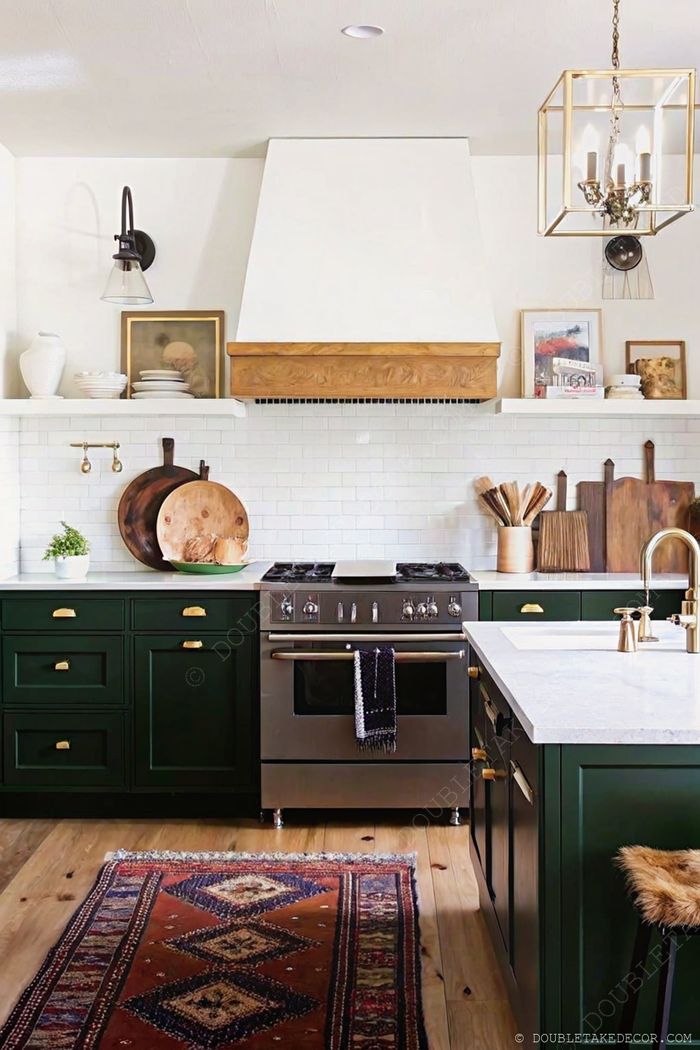 Modern kitchen with deep green cabinets, white subway tile, wooden hood, and decorative cutting boards creating a functional yet stylish space.