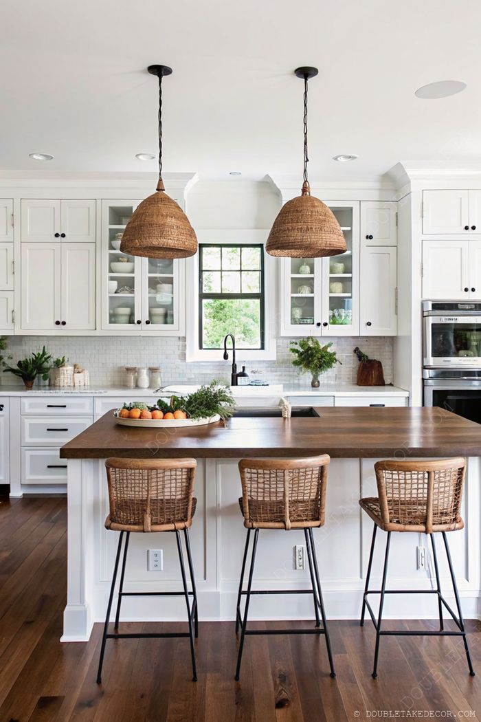 White kitchen with dark wooden island countertop, woven pendant lights, and decorative fruit tray, creating a modern rustic aesthetic.