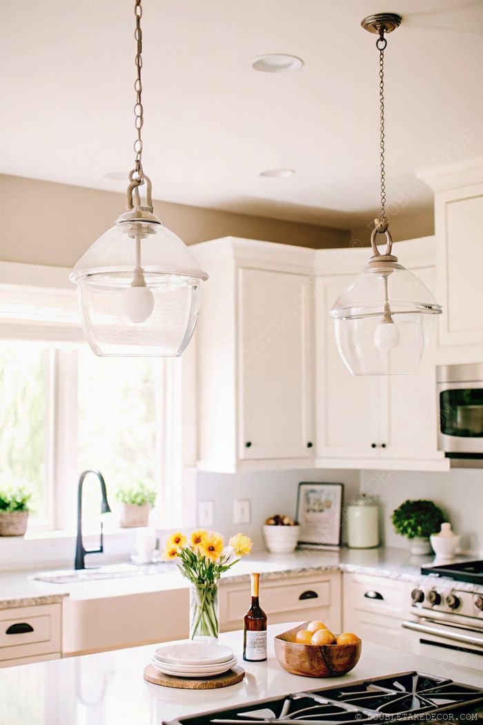 Bright kitchen with glass pendant lights, wooden serving board, yellow flowers, and fresh oranges creating an elegant, inviting space