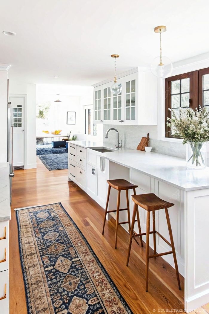 Bright kitchen with white glass-front cabinets, marble countertops, wooden bar stools, and elegant pendant lights over the island.