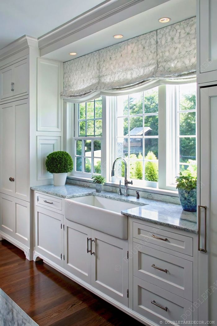 Bright kitchen with white cabinets, marble countertop, farmhouse sink, and decorative potted plants near sunlit windows.